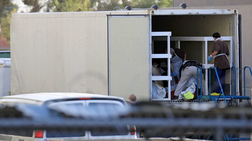 Medical workers are seen in one of three refrigerated trailers.