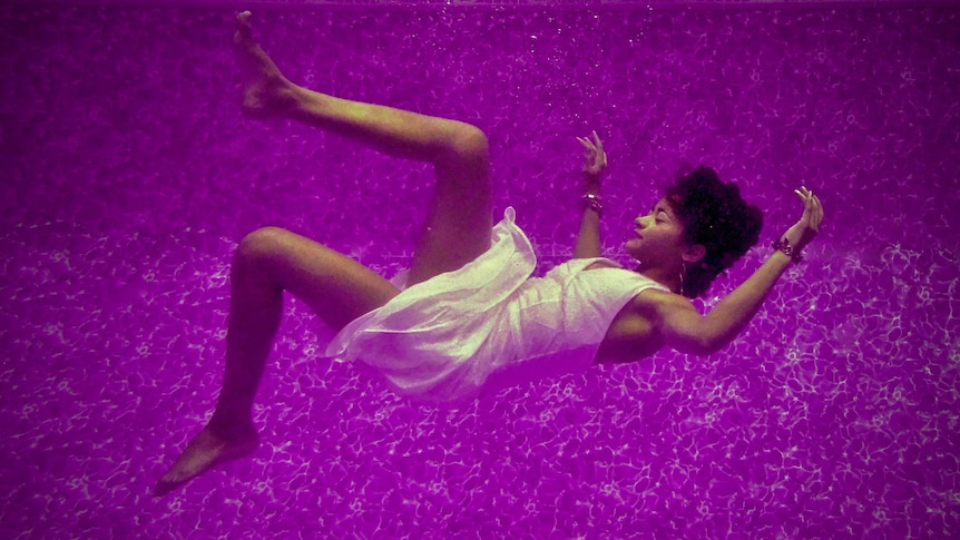 A woman in a white dress falling on her back on a purple background.