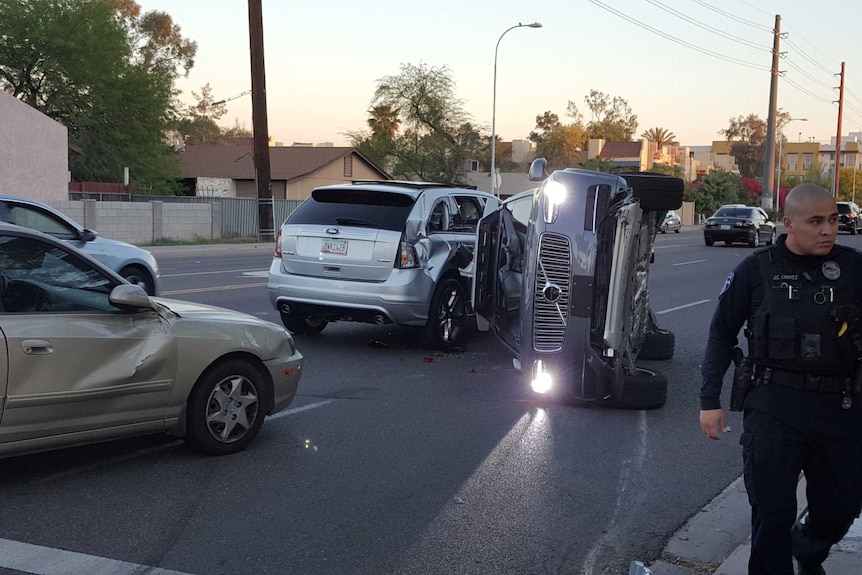 A police officer walks away from a crash site with a volvo on its side and two other dinted cars.