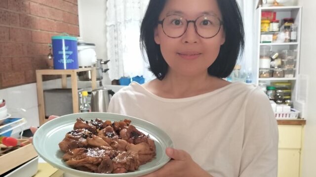 Liling Xu stands in a kitchen, holding out a plate of succulent chicken that she has cooked.