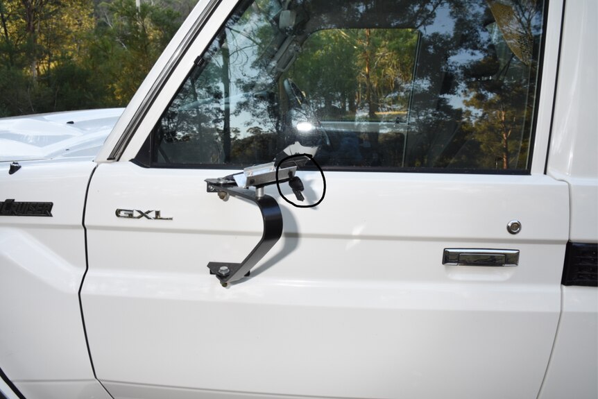 A close-up shot of the passenger side of a white ute, which depicts damage to the mirror.