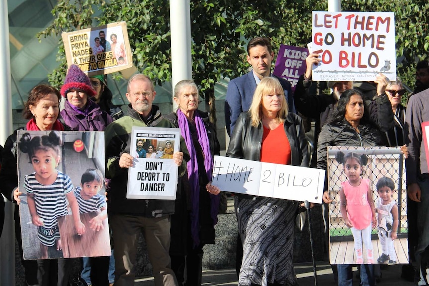 About 12 people stand outside the court, holding photographs and placards in support of the Tamil family.