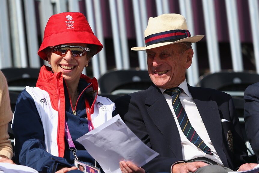 Princess Anne in sunglasses and a bucket hat sits next to her father Prince Philip.