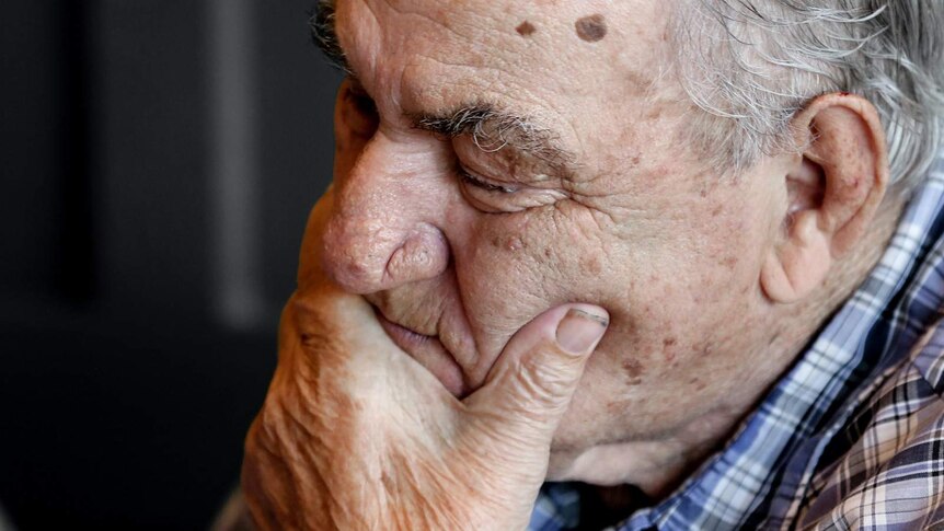 An elderly man holds his chin with his eyes closed.