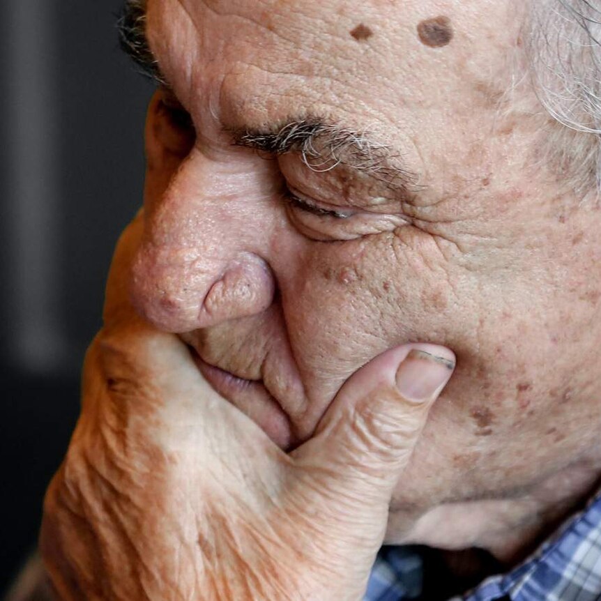 An elderly man holds his chin with his eyes closed.