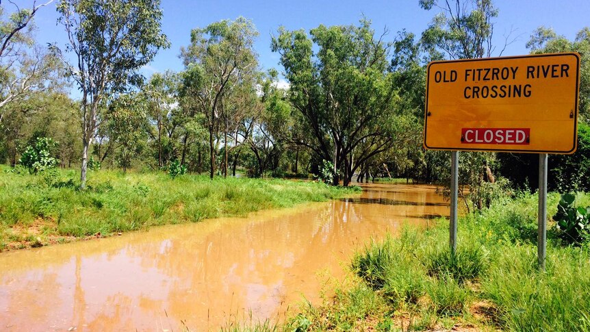 Brown water covers the flooded Old Fitzroy River crossing with a yellow sign on the right.