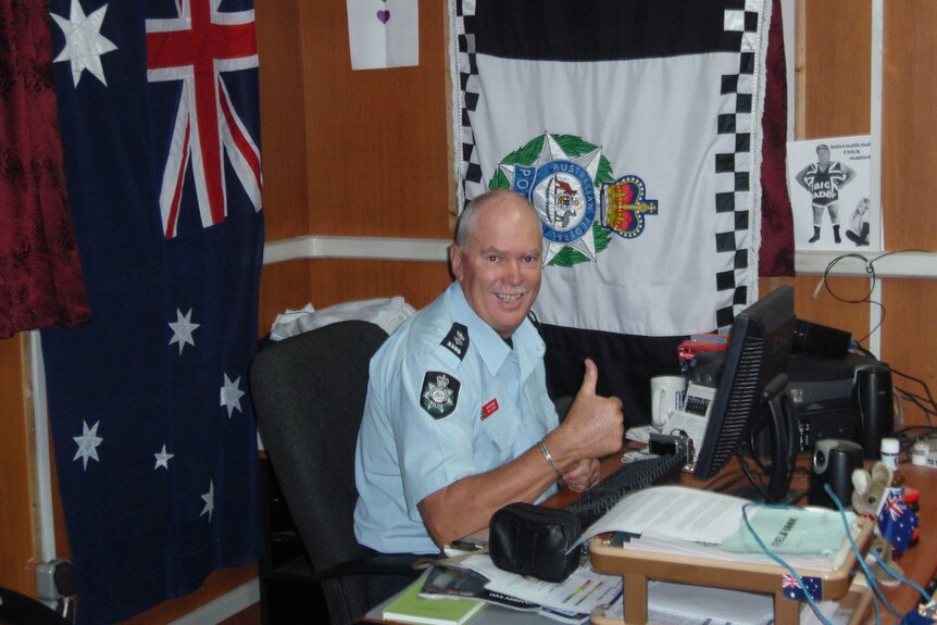 A man in an AFP uniform sits in an office with the Australian and AFP flags behind him.