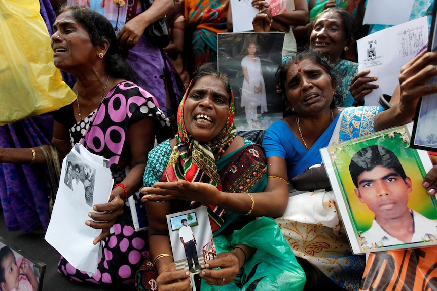 A group of ethnic Tamil women look anguished holding up pictures of family members and crying
