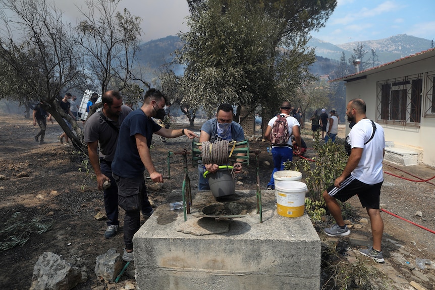 Group of volunteers gathers water with a small bucket from an old well