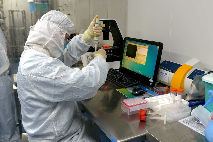 A man in full PPE injecting something into a test tube while another man watches