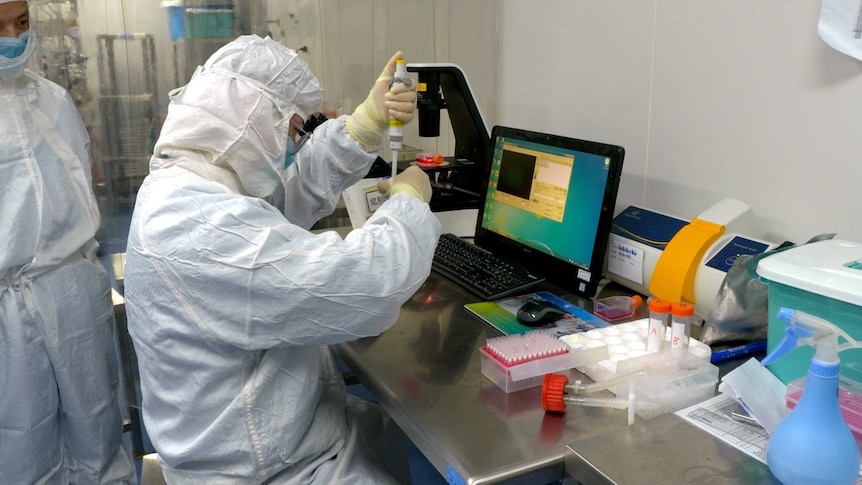 A man in full PPE injecting something into a test tube while another man watches