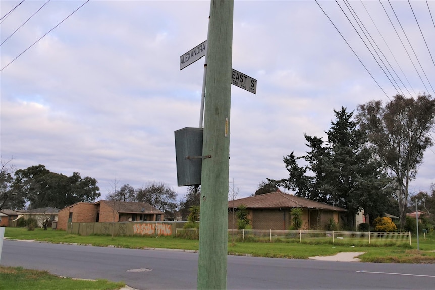 A corner street sign with signs for both East and Alexandra streets, with derelict houses in the background