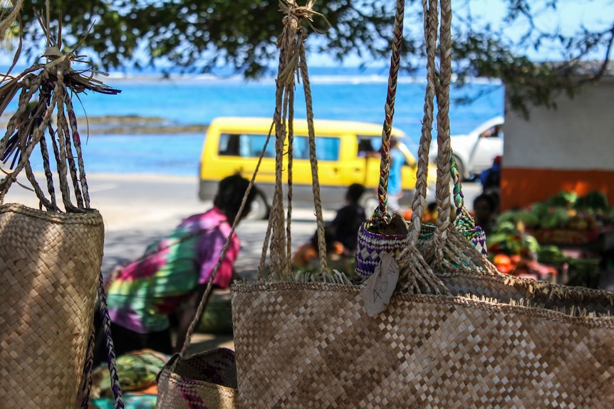 A bright yellow van and farmer's markets are seen through woven handbags on a Pacific island.