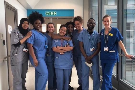 A group of people in various shades of blue and grey scrubs, standing in a hospital hall.