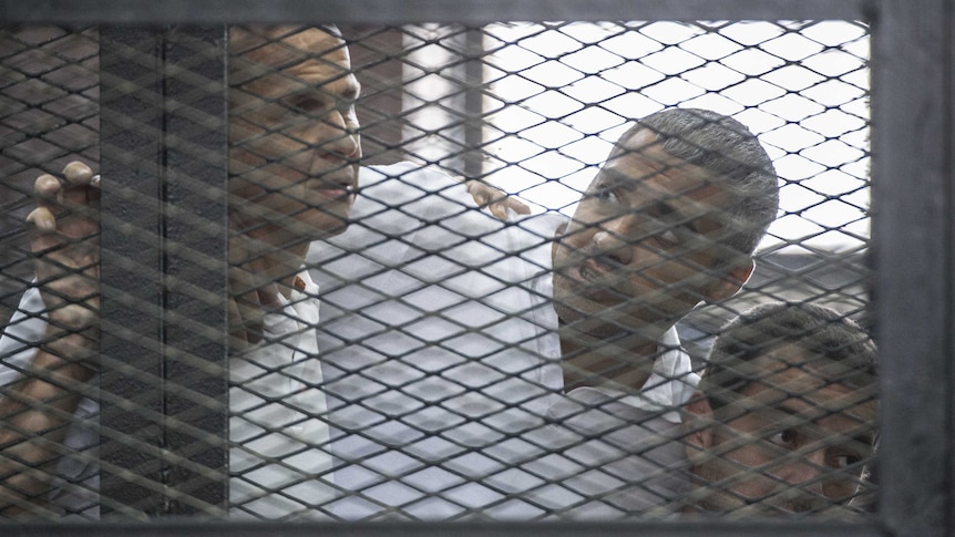 Peter Greste and his colleagues listen to the verdict inside the defendants cage