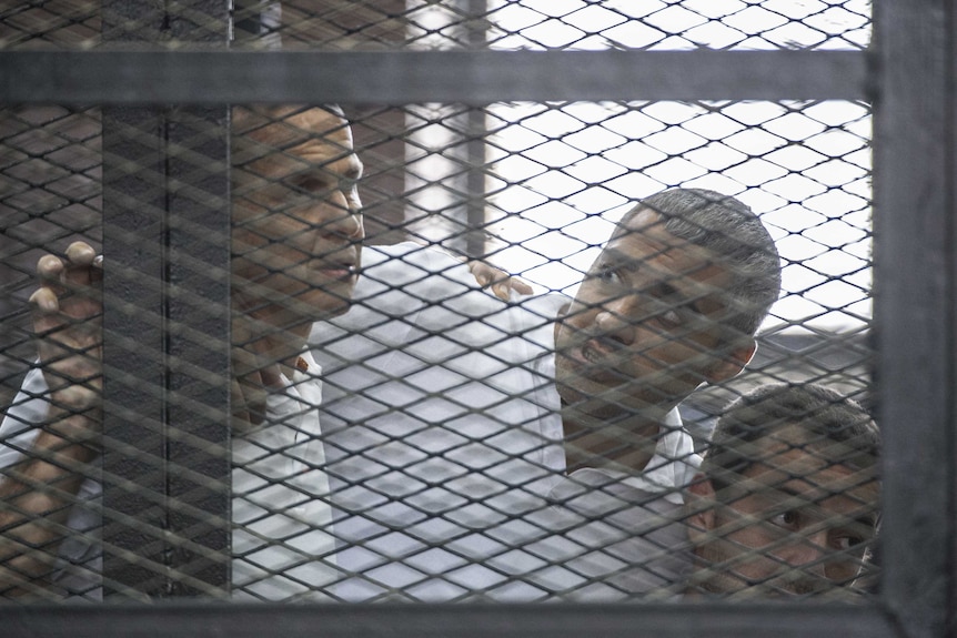 Peter Greste and his colleagues listen to the verdict inside the defendants cage