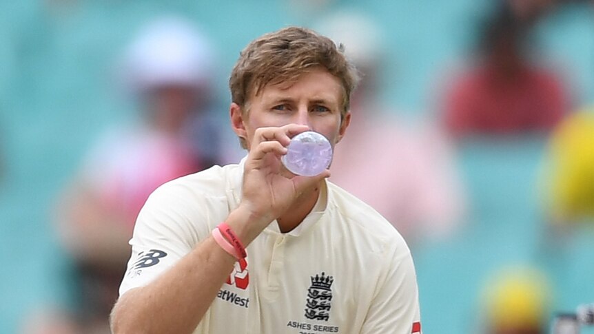 Joe Root squats as he takes a drink from a water bottle
