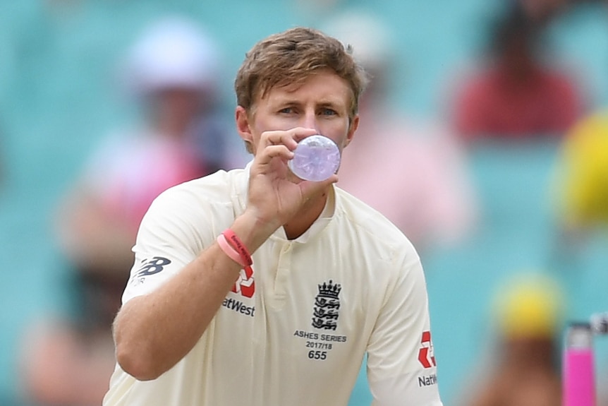 Joe Root squats as he takes a drink from a water bottle