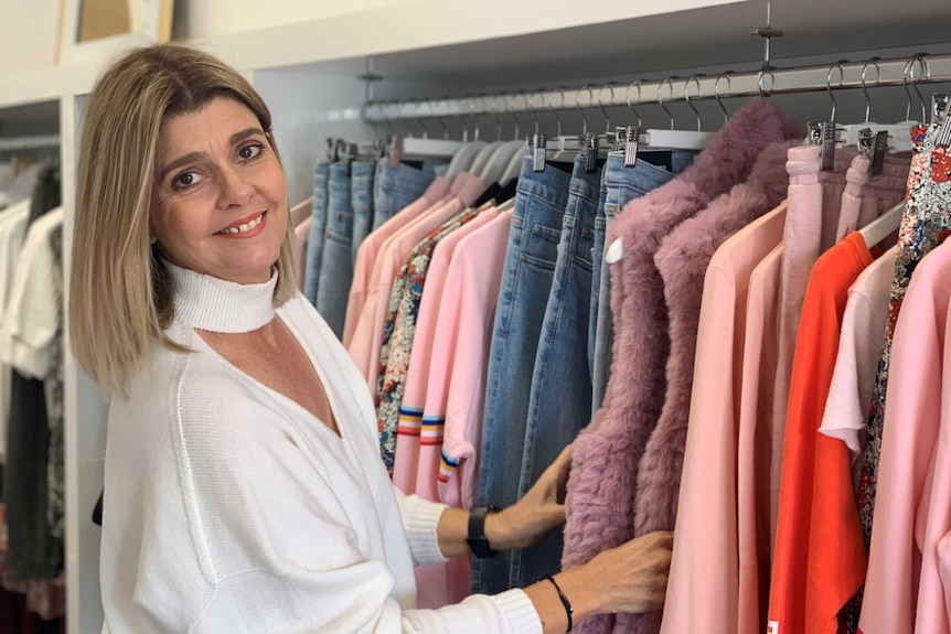 A lady standing in front of a clothes rack sorting through bright coloured clothes in a women's fashion boutique.