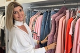 A lady standing in front of a clothes rack sorting through bright coloured clothes in a women's fashion boutique.
