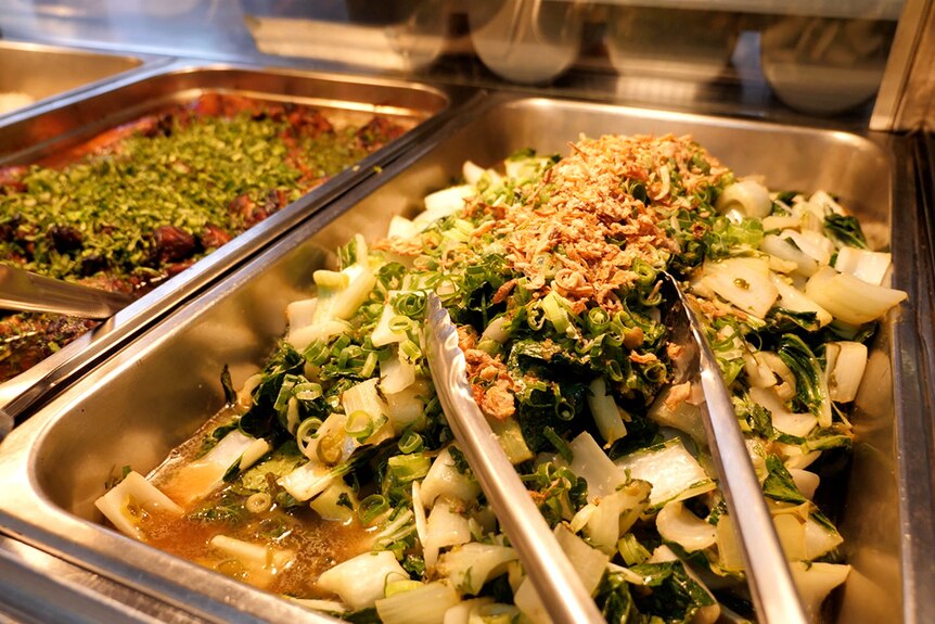 A metal tray of green Asian vegetables under a warm heating lamp