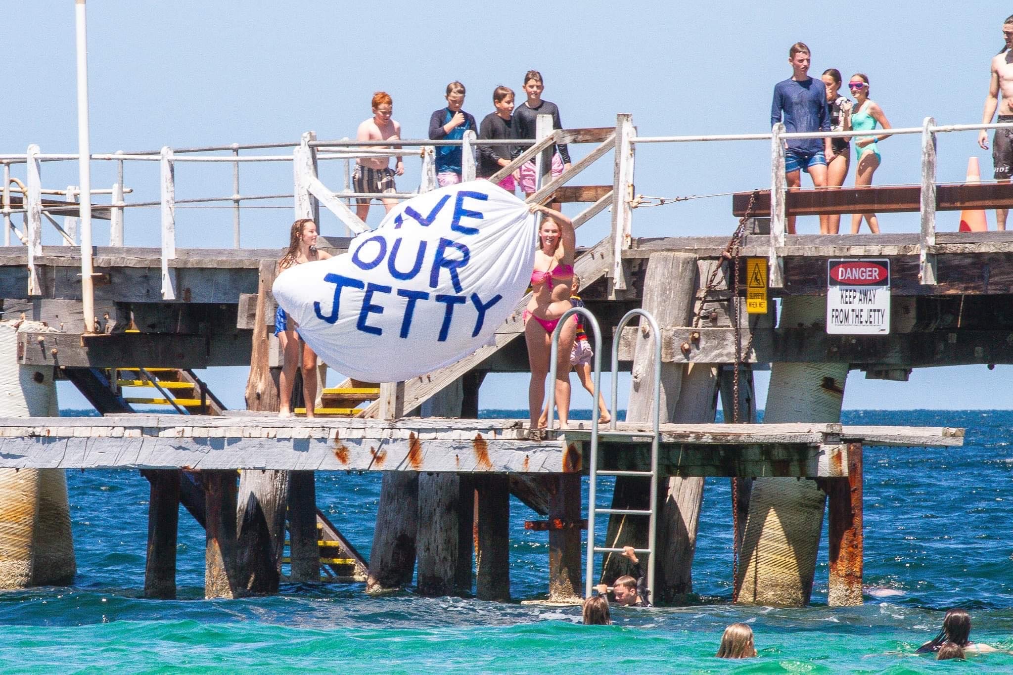 two teenage girls holding save our jetty sign on platform of jetty