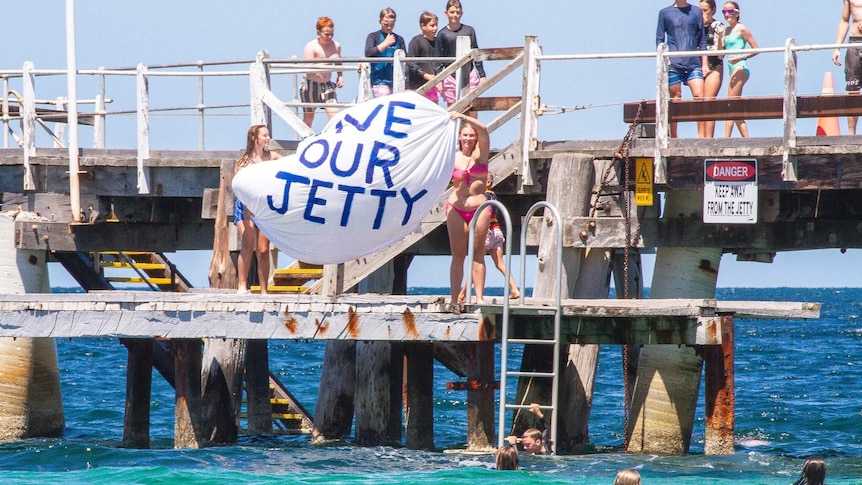two teenage girls holding save our jetty sign on platform of jetty
