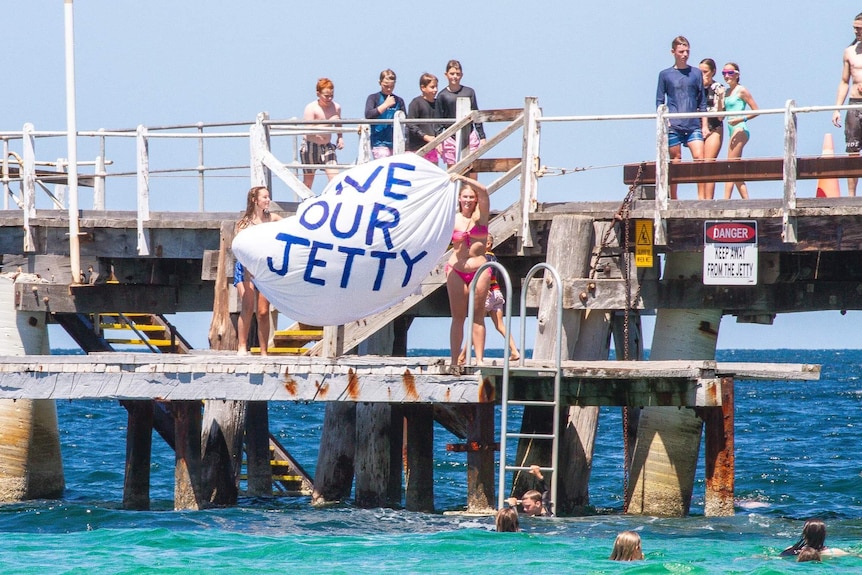two teenage girls holding save our jetty sign on platform of jetty