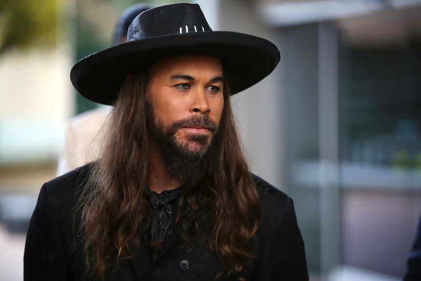 A man with long hair and a cowboy hat looking deep in thought.