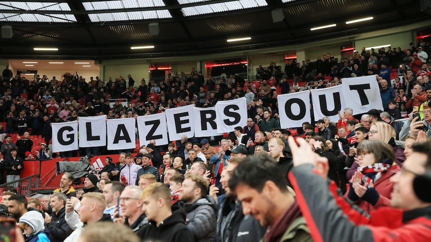 Fans hold up signs spelling GLAZERS OUT inside a stadium