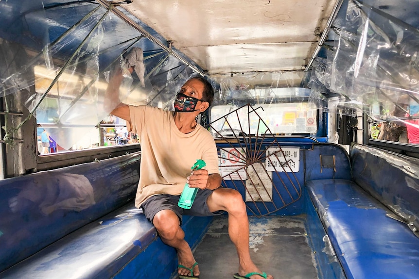 A man in a face mask cleans the inside of a vehicle with a spray bottle and towel