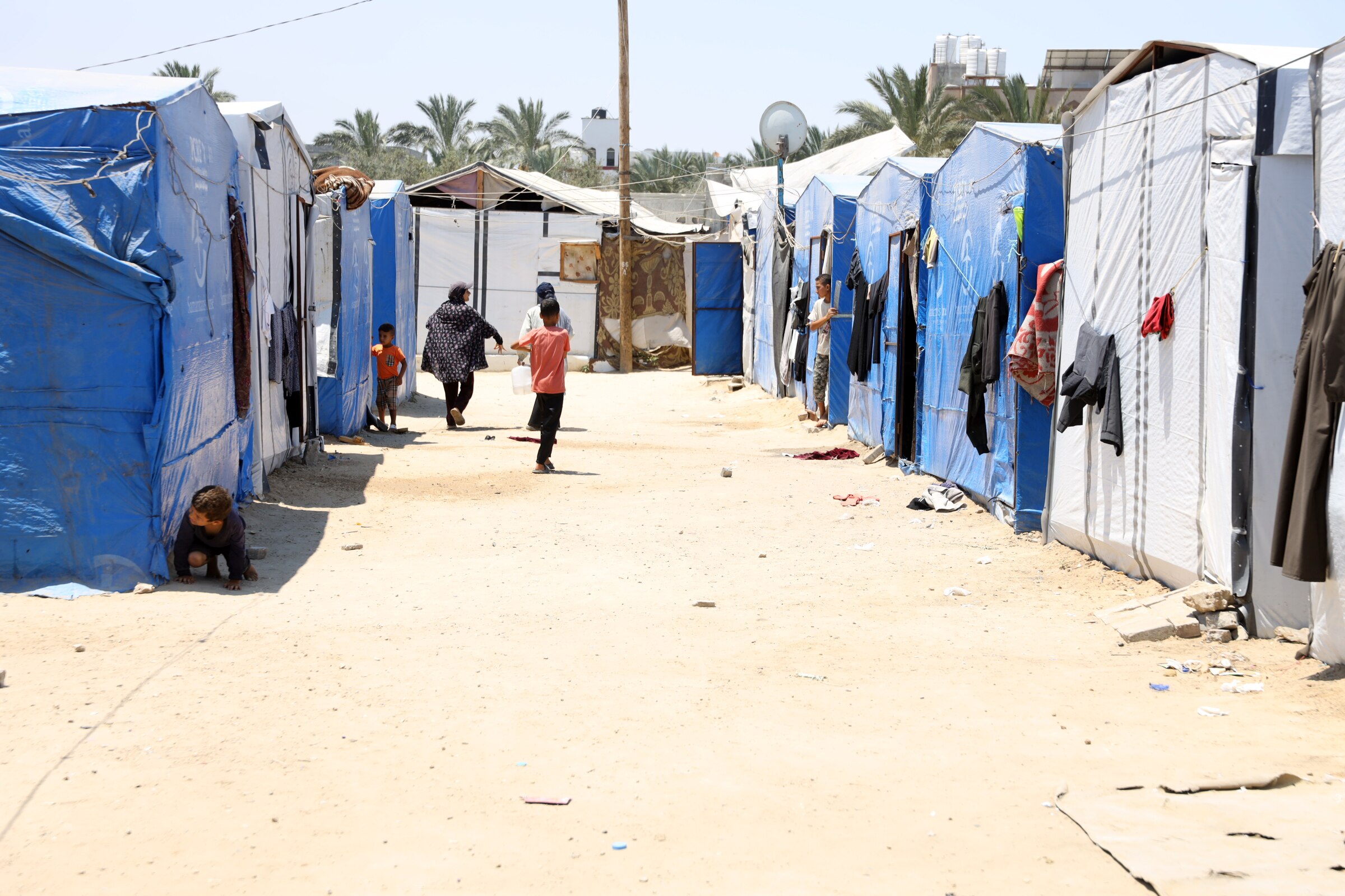 Children run over dusty ground between tents made from blue tarpaulins.