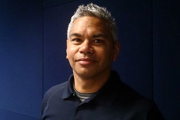 Studio-style posed shot of man wearing casual shirt against blue background.