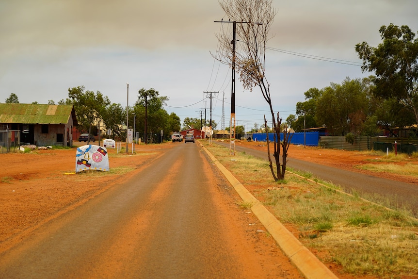 A small town street lined by red dirt. To one side is a car bonnet decoratively painted as a "40" sign.