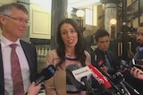 NZ Labour leader Jacinda Arden at a press conference, surrounded by reporters with microphones.