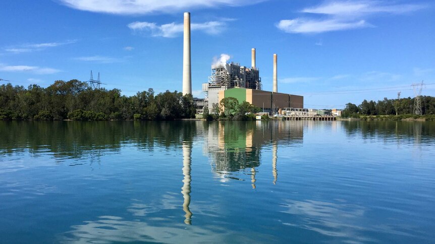 Vales Point Power Station sits to the right of image over lake on a clear blue day. Smoke comes out of building.