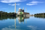 Vales Point Power Station sits to the right of image over lake on a clear blue day. Smoke comes out of building.