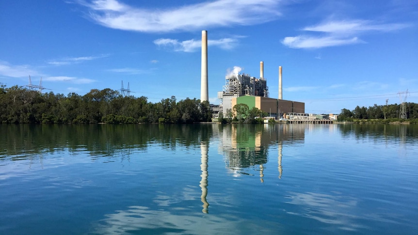 Vales Point Power Station sits to the right of image over lake on a clear blue day. Smoke comes out of building.