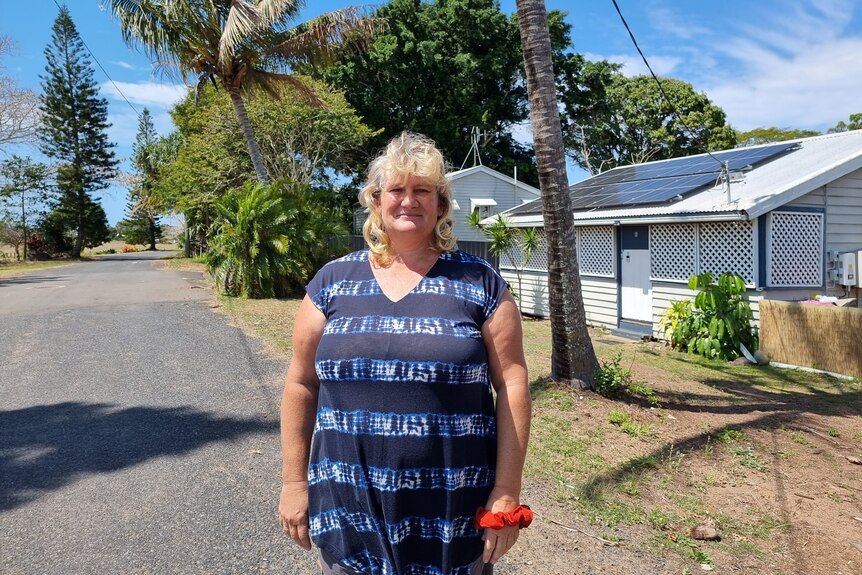 A woman stands in the street in front of a home.