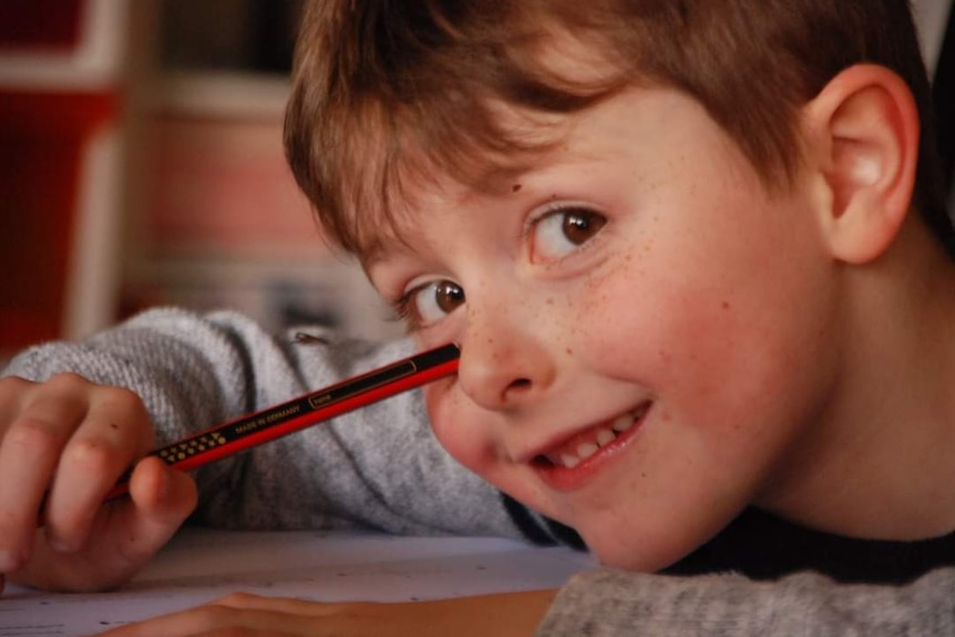 A close up of a young boy holding a pencil and smiling at the camera