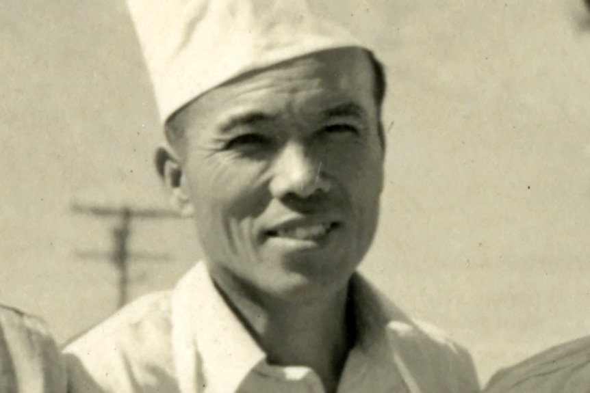 A black and white photo of a Japanese man, he is smiling