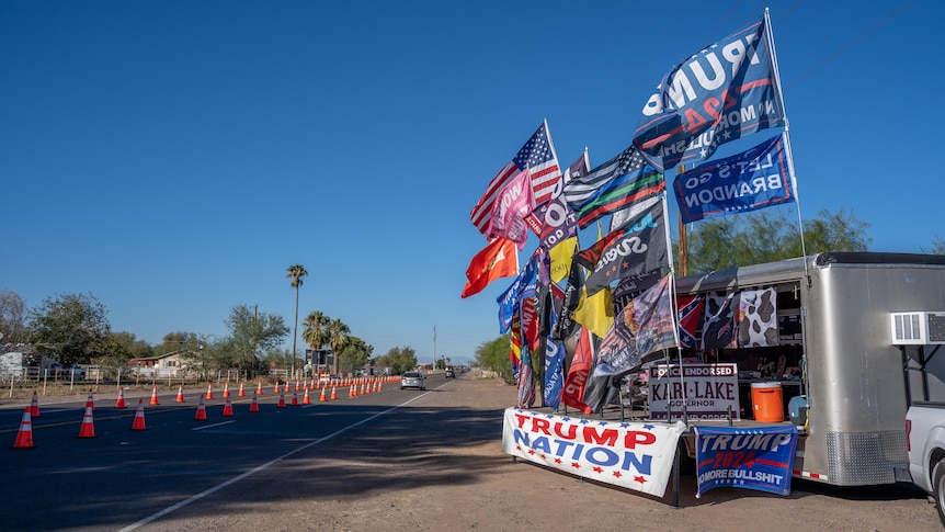 A truck kitted out with TRUMP NATION and KARI LAKE signs and flags sits by the roadside