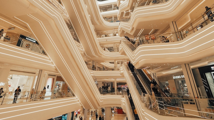 The interior of a Chinese mall with white escalators and neon lights. 