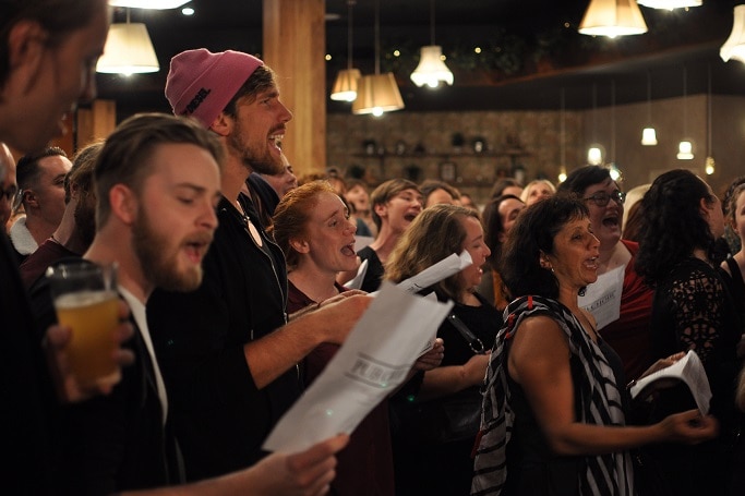 Singers with lyric sheets and beers in their hands.