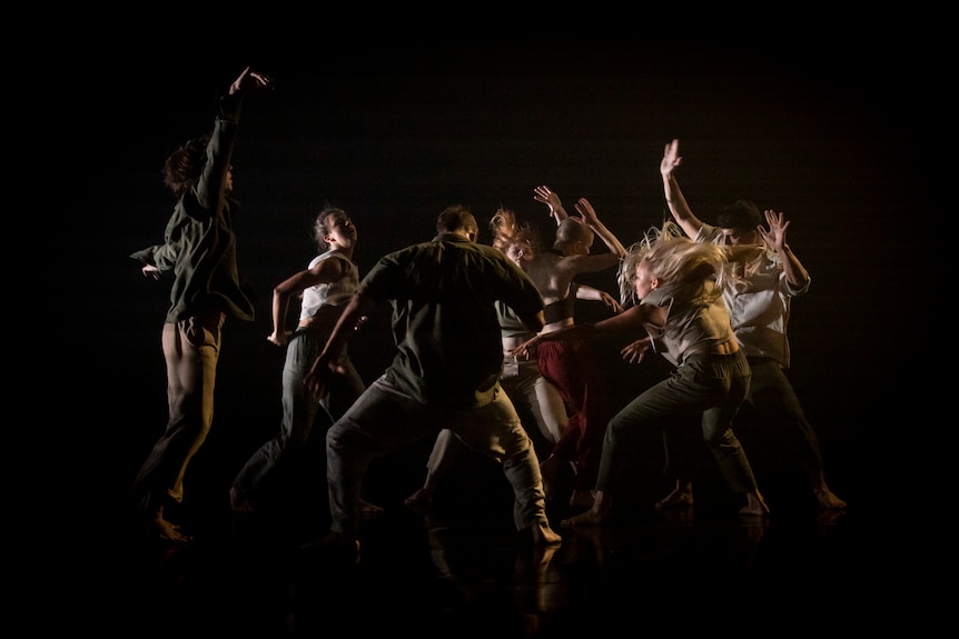 A group of dancers thrash around in a circle on a darkened stage.