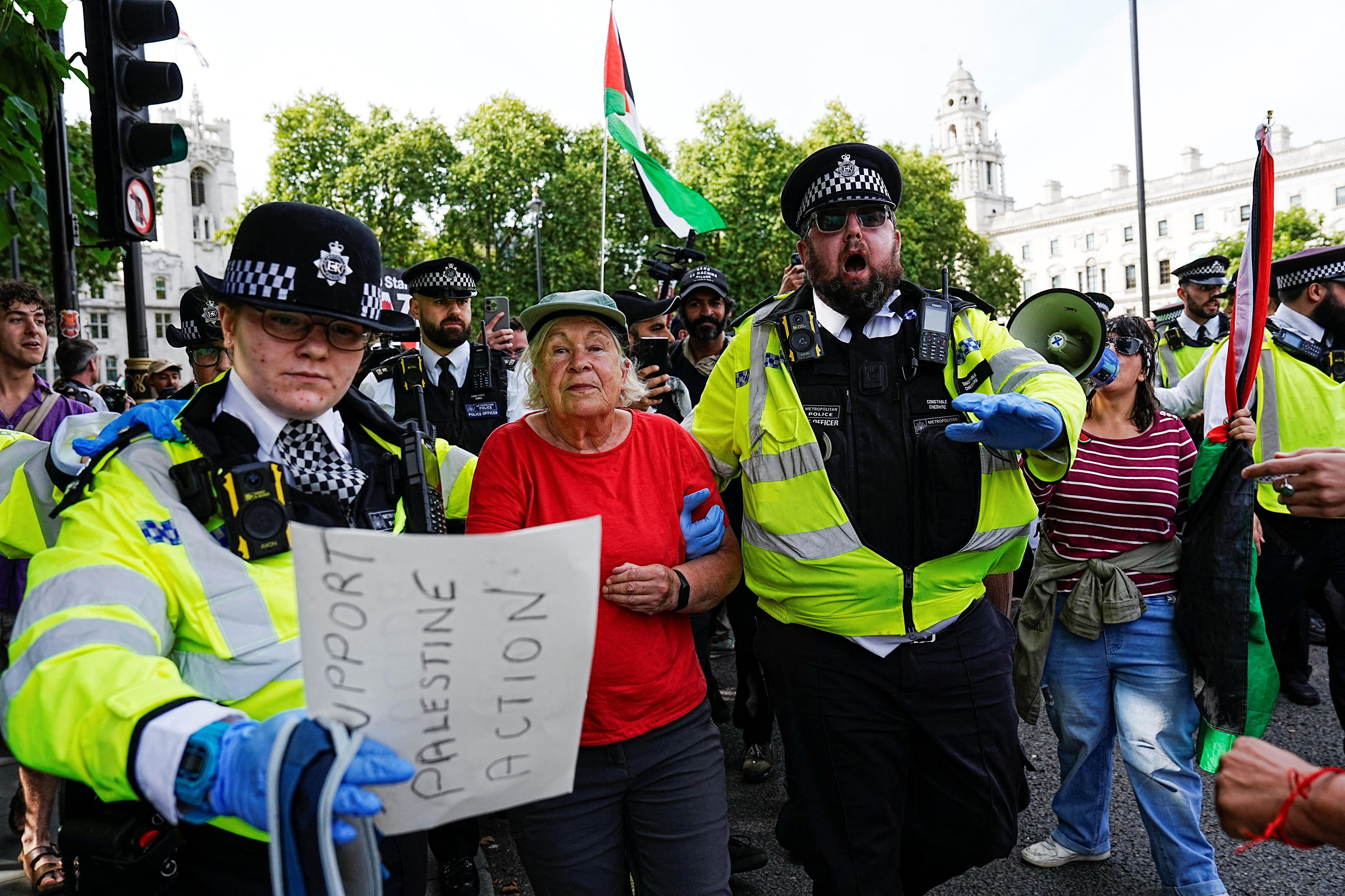 A woman wearing a red tshirt being moved along by police officers during a protest.