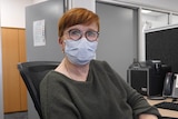 Kathy Seward sitting at a desk with a mask on.