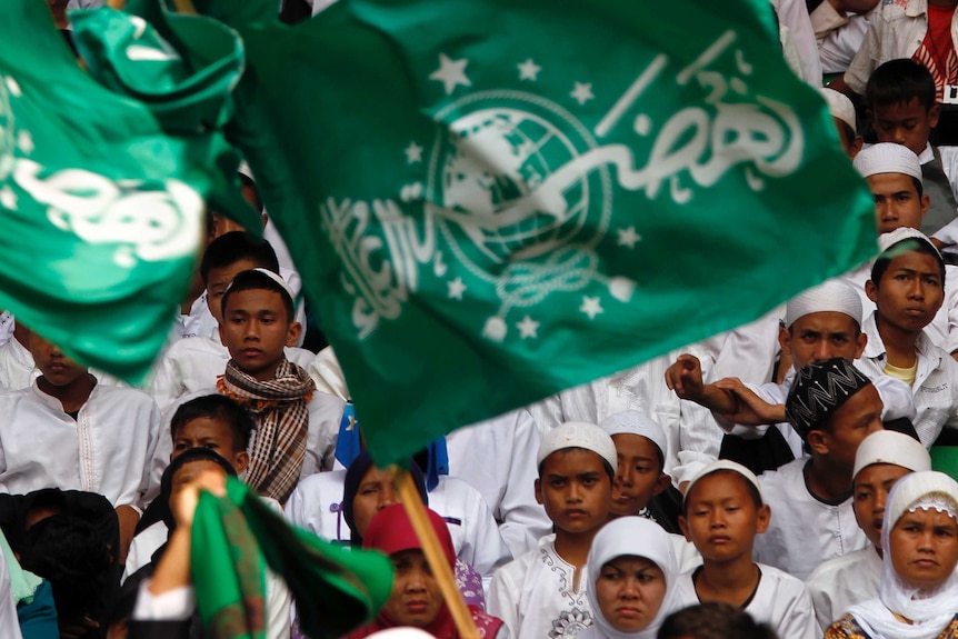 un groupe de personnes apporte un grand drapeau avec des lettres arabes