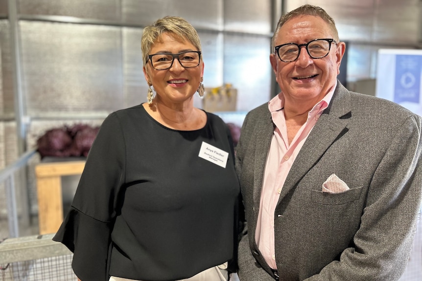 A woman with short blonde hair and glasses standing next to a man with short hair and glasses