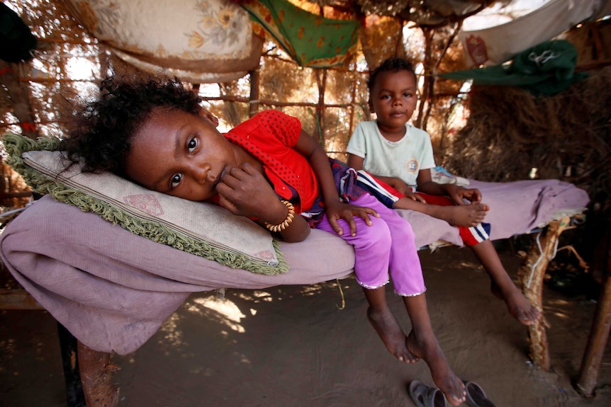 Children rest on a bed at their family hut